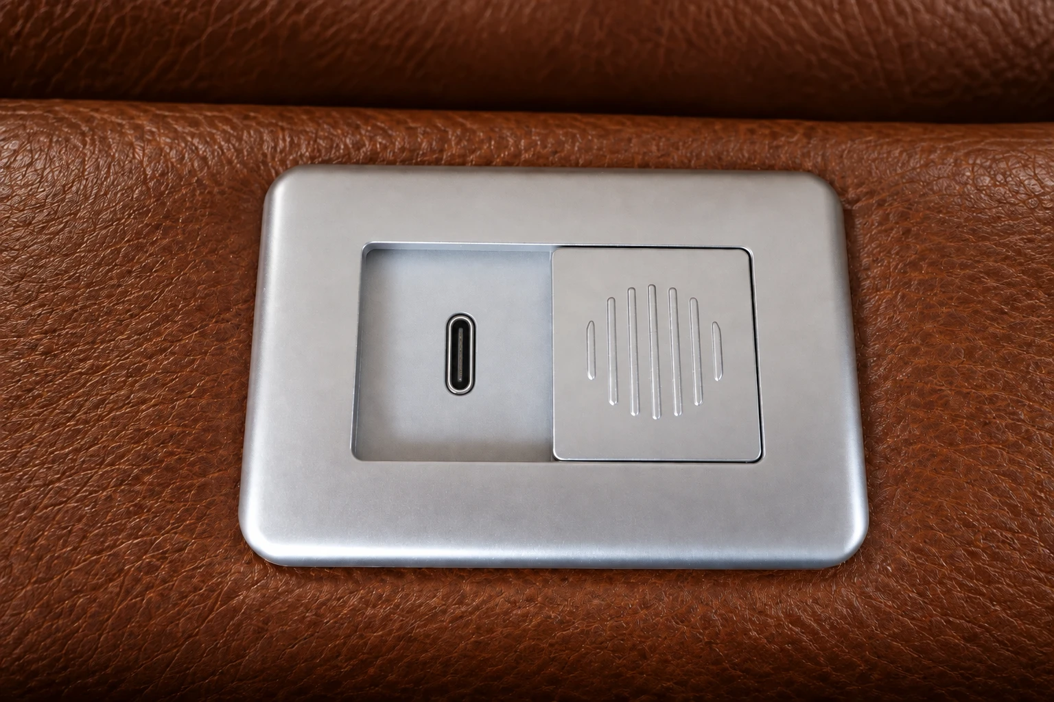 Poglądowy detal pojedynczego gniazda USB-C z przesuwną osłoną w skórzanej tapicerce